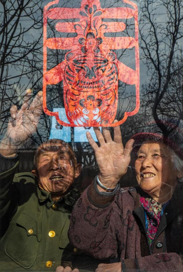 臘月里，霍州市師莊鄉(xiāng)馮南垣村村民師榮光(左)在災(zāi)后重建的新家里貼窗花。(霍州市委宣傳部供圖)