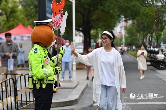 6月7日上午9時(shí)，隨著鈴聲的響起，2023年江西高考正式開考，江西省的53.57萬(wàn)考生以縣（區(qū)）為單位隨機(jī)安排在全省256個(gè)考點(diǎn)、18968個(gè)考場(chǎng)參加高考。圖為“小熊交警”和考生擊掌鼓勵(lì)。 人民網(wǎng)記者 時(shí)雨攝