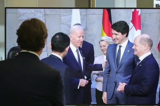 2022年3月24日，在比利時布魯塞爾的北約總部，一名男子觀看屏幕上美國總統(tǒng)拜登（右四）、歐盟委員會主席馮德萊恩（右三）、加拿大總理特魯多（右二）、德國總理朔爾茨（右一）出席七國集團峰會合影儀式的畫面。新華社記者鄭煥松攝