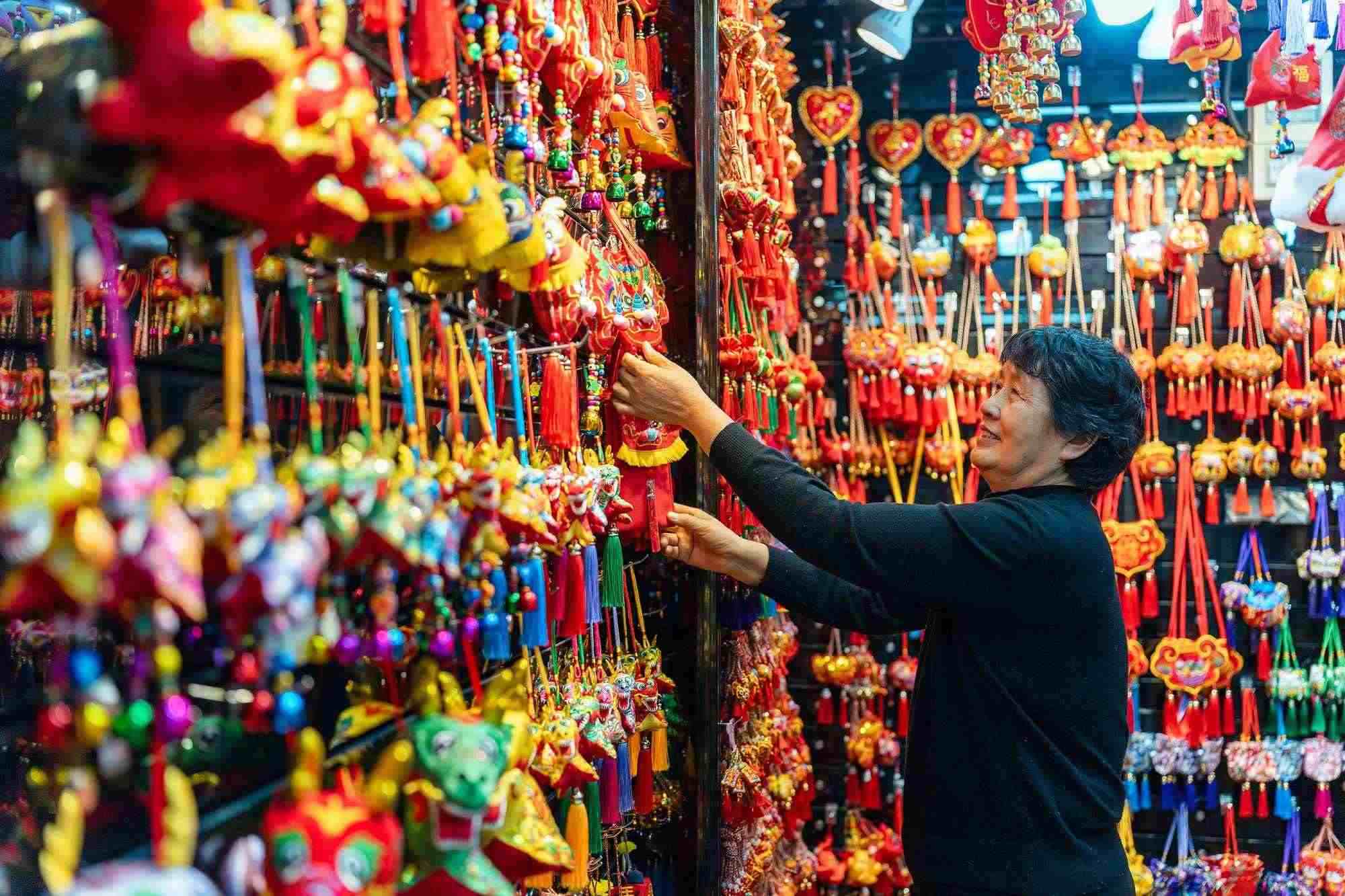 2023年12月11日，金華義烏國際商貿(mào)城，龍年喜慶用品掛滿攤位，顧客正在挑選中。