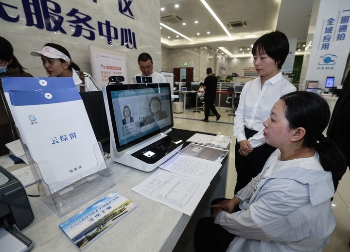 在浙江省嘉興市秀洲區(qū)王江涇鎮(zhèn)便民服務(wù)中心的“跨域通辦·云綜窗”窗口，辦理開業(yè)登記的個(gè)體工商戶（右一）通過該系統(tǒng)與江蘇省蘇州市吳江區(qū)盛澤鎮(zhèn)行政審批局工作人員視頻連線，進(jìn)行身份讀取及材料線上審核（2024年5月9日攝）。新華社記者 徐昱 攝