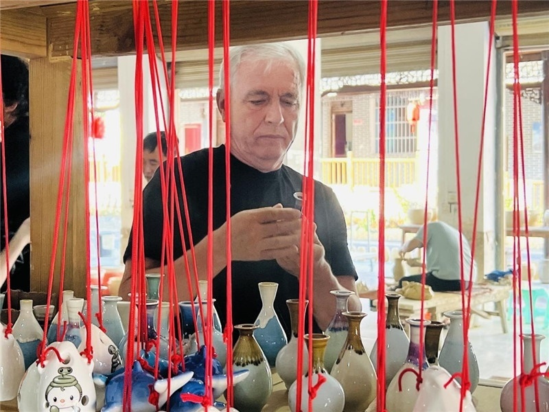 鄉(xiāng)愁如同一根根紅線，將游子與故鄉(xiāng)永遠(yuǎn)地牽連到一起。花茂村陶藝文化創(chuàng)意一條街的母氏陶藝館內(nèi)，紅線吊著陶瓶，思緒游走萬(wàn)里。摩爾多瓦“信息標(biāo)簽”通訊社社長(zhǎng)亞歷山大·塔納斯端詳著館內(nèi)展示的陶藝作品，并挑選出心儀的小擺件帶回摩爾多瓦，也帶走花茂村的“鄉(xiāng)愁”。（張亞欣攝）