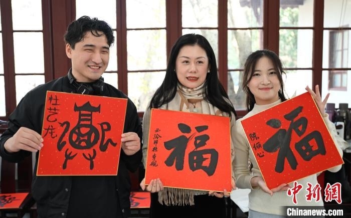 1月20日，外籍留學生和西泠印社社員李硯(中)展示各自創(chuàng)作的福貼。當日，來自巴西、馬來西亞、加納、哈薩克斯坦的外籍留學生在浙江杭州西泠印社體驗福貼、春聯和篆刻，感受古老的中國傳統文化。中新社記者 王剛 攝
